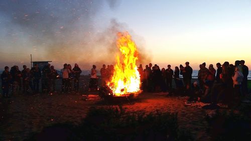 People standing by bonfire at dusk