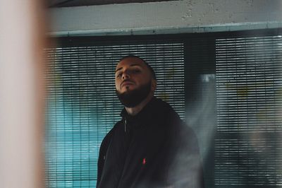 Portrait of man with beard standing against window at home