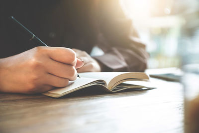 Midsection of woman writing in book at table