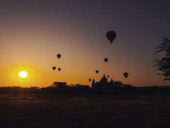 Silhouette hot air balloons on field against sky during sunset