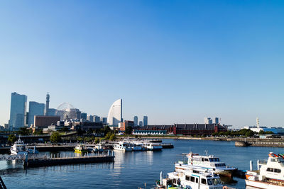 Boats in harbor against clear sky in city
