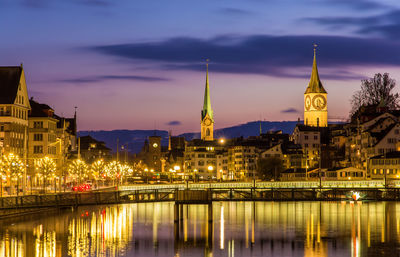 Illuminated buildings by river against sky at night