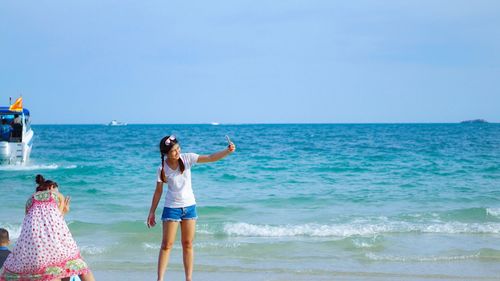 Friends standing on beach against clear blue sky