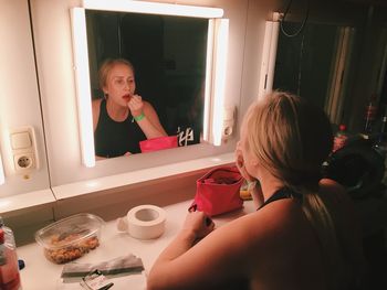 Reflection of woman in mirror while applying lipstick