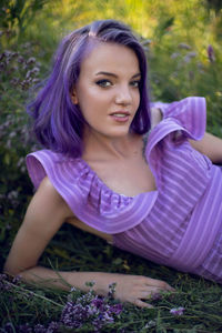 Teenage girl with dyed purple hair and a nose piercing in the grass  in a short dress