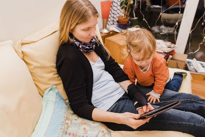 High angle view of woman showing digital tablet to daughter while sitting on sofa at home