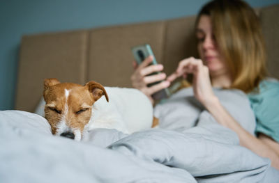 Woman with dog chilling on bed, use smartphone