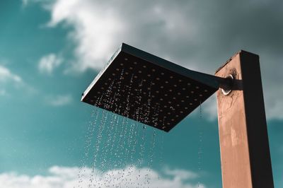 Low angle view of pool shower against cloudy sky