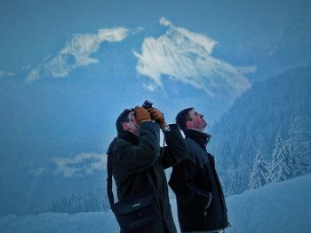 Mid adult man by friend photographing on snowcapped mountain