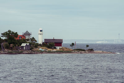 Lighthouse amidst sea and buildings against sky