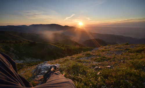 Low section of person on landscape against sky during sunset