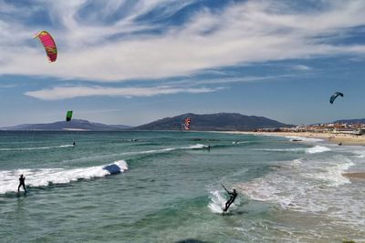 People kiteboarding in sea against cloudy sky