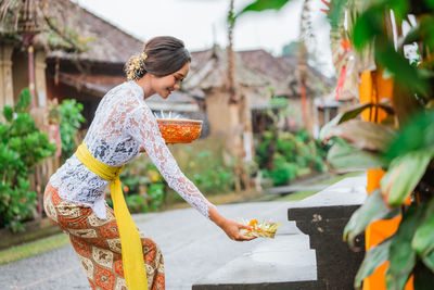 Side view of young woman standing against plants