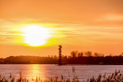 Silhouette trees by lake against orange sky