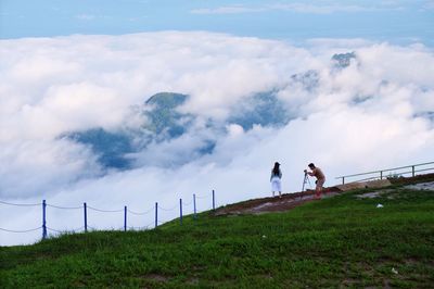 Man photographing woman on field against sky