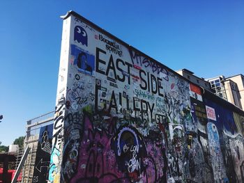 Low angle view of graffiti on building against blue sky - east side gallery berlin 