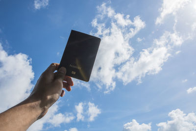 Cropped image of person holding passport against sky