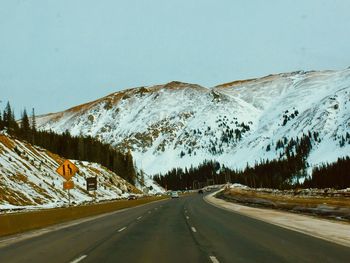 Empty road amidst snowcapped mountains against clear sky