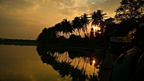 Silhouette palm trees by lake against sky during sunset