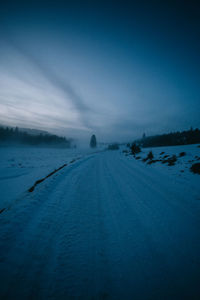 Tire tracks on road against sky during winter