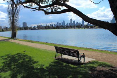 Empty bench by river at park against sky