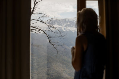 Rear view of woman looking through window at home