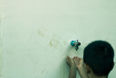 Close-up of boy with hands cupped on faucet against wall