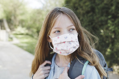 Girl wearing mask while standing with backpack