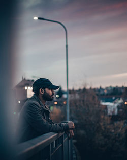 Side view of young man standing against sky in city