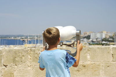 Rear view of boy standing by cityscape against sky