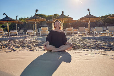 Portrait of smiling mature woman sitting at sandy beach during sunny day