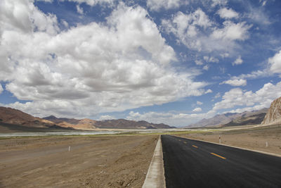 A flat, newly built wide asphalt road leads to the beautiful mountains in the distance