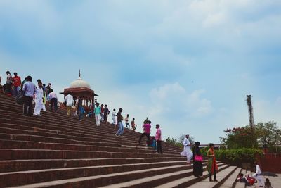 People walking on staircase against cloudy sky