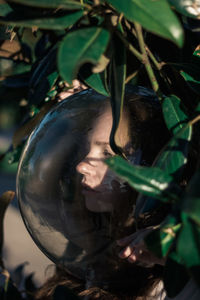 Close-up of young woman wearing glass ball on head amidst leaves