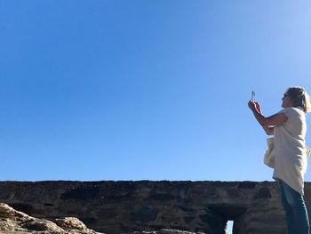 Low angle view of woman photographing against clear blue sky