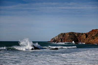 Waves splashing on rocks by sea against sky