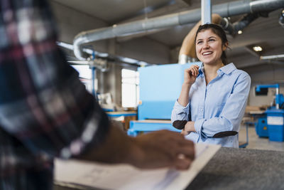 Smiling businesswoman working with colleague while standing at industry