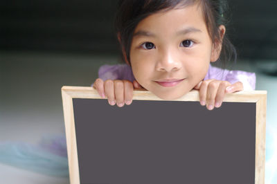 Portrait of cute girl holding writing slate at home