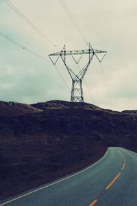 Electricity pylon by road against sky