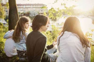 Teenagers sitting at lakeshore on sunny day