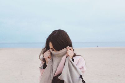 Woman covering face at beach against sky