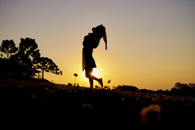 Silhouette man walking on field against sky during sunset