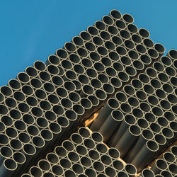 Low angle view of pipe stacked against clear blue sky