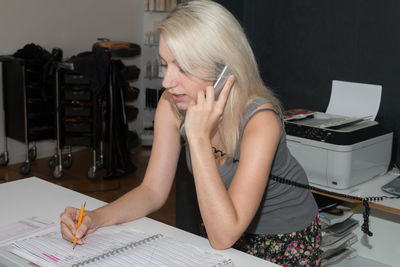 Young blond woman talking on landline phone while working at desk in office
