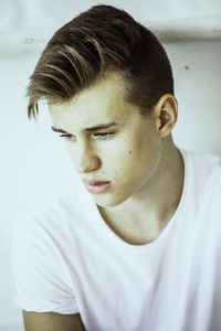 Thoughtful young man looking away while sitting against wall