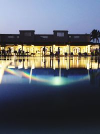 Illuminated building by river against sky at night