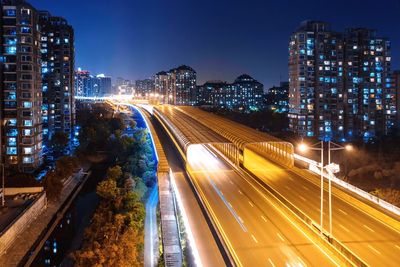 High angle view of light trails on road amidst buildings in city at night