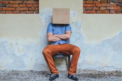 Man wearing cardboard box with attitude expression against wall