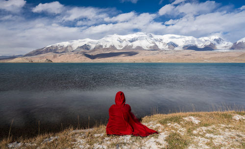 A person in red cloak is looking at snow mountains.