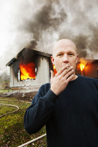 Man smoking cigarette in front of burning building